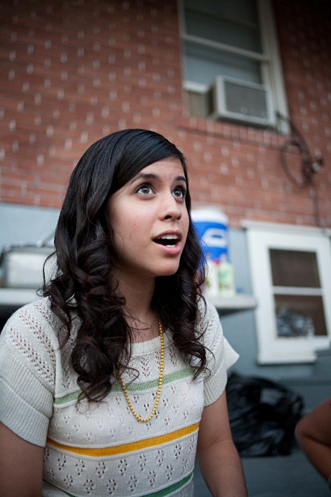 Ashly Burch, cheveux bruns ondulés, regarde vers le haut devant un mur de briques