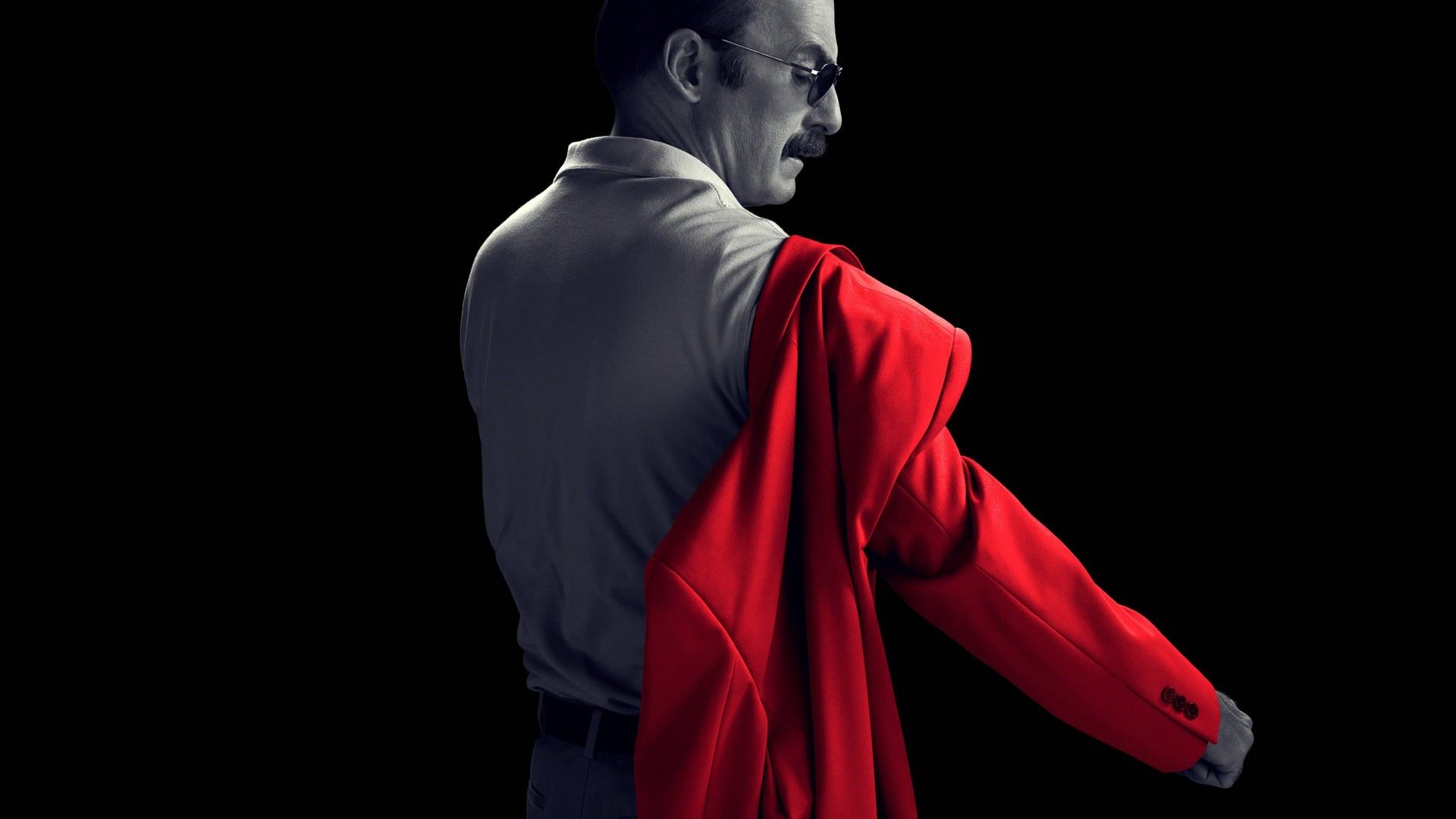 Saul Goodman, de dos et en noir et blanc, enfile une veste rouge vif sur un fond noir.