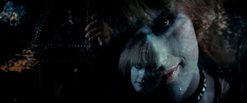 Pris, jouée par Daryl Hannah, le visage poudré de blanc et les yeux cernés de noir, sourit dans la pénombre, une main posée sur une paroi.