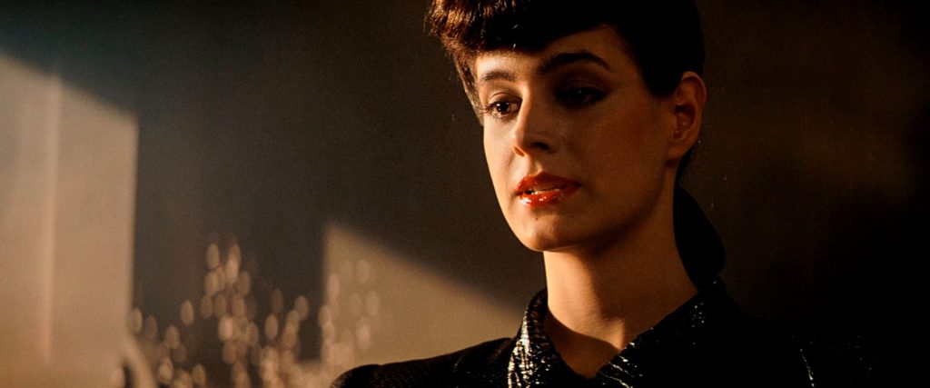 Rachael, jouée par Sean Young, cheveux bruns relevés et rouge à lèvres, dans une pièce baignée de lumière orangée.