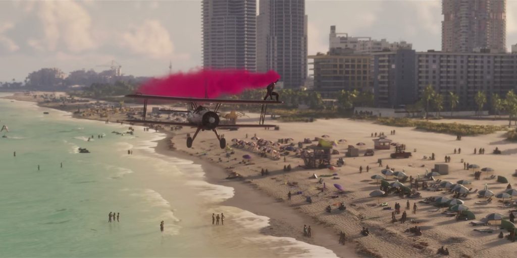 Un biplan traîne une fumée rose au-dessus d'une plage bondée, bordée de tours et de palmiers.
