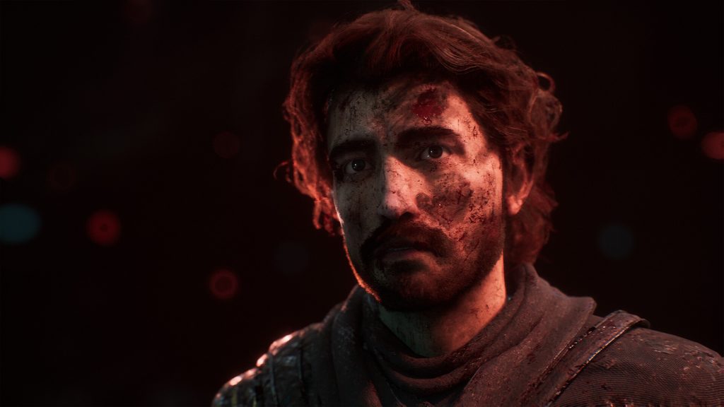 Gros plan sur le visage d’un homme barbu, le front et la joue couverts de sang, dans une lumière rouge.