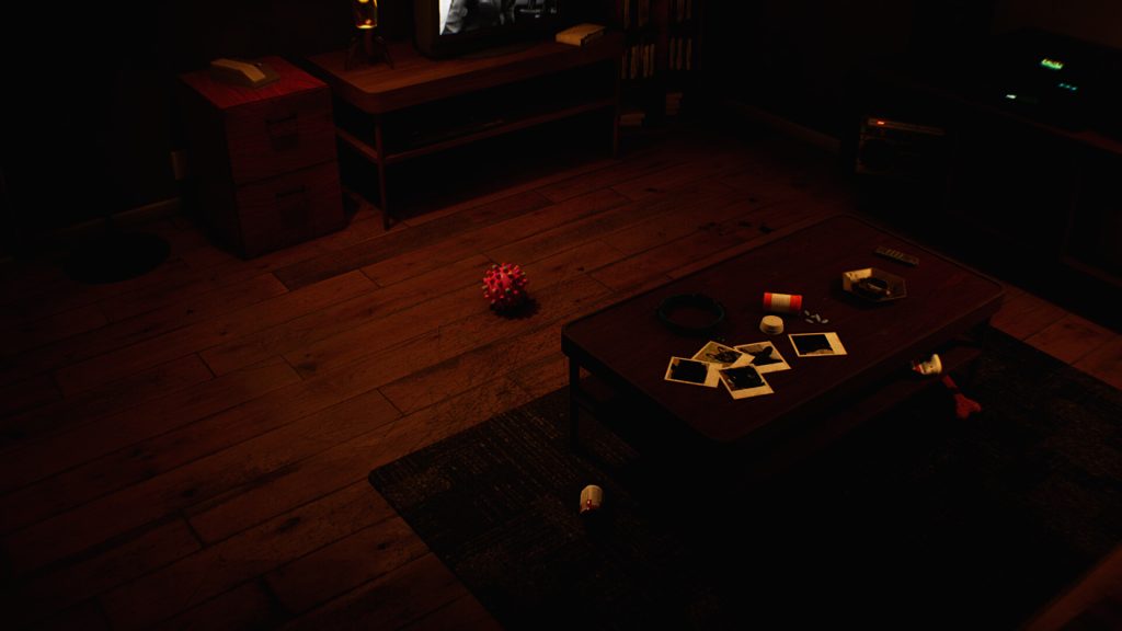 Un salon dans la pénombre : parquet, télévision allumée sur une image en noir et blanc, et une table basse couverte de photos instantanées, d’un flacon de médicaments et d’un cendrier. Une balle rouge à picots traîne par terre.