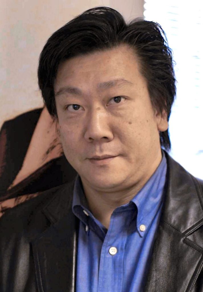 Hiromichi Tanaka, cheveux noirs, en veste de cuir sur une chemise bleue.