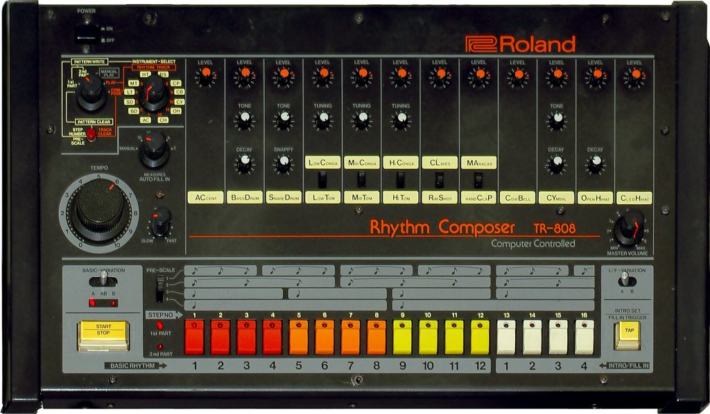 Une boîte à rythmes Roland TR-808, panneau gris couvert de boutons rouges, orange et jaunes, et de potentiomètres.