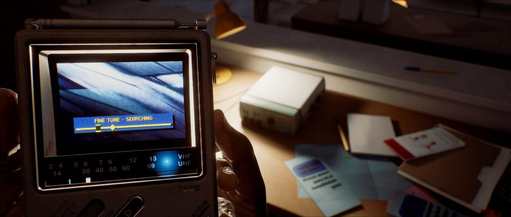Une télévision portable affiche « Fine tune, searching » au-dessus d'un bureau éclairé par une lampe, couvert de papiers et de cartes.