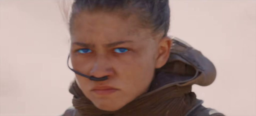 Gros plan sur Zendaya en Chani, les yeux bleus, un tube de distille sous le nez, dans la lumière pâle du désert.