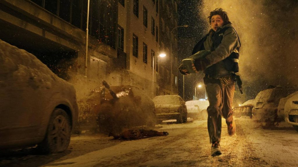 Un homme court dans une rue enneigée la nuit, entre des voitures couvertes de neige, sous la lumière des lampadaires.