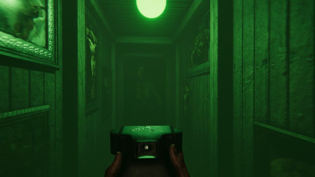 Deux mains tiennent l’appareil photo instantané dans un couloir lambrissé baigné de lumière verte ; au fond, une forme sombre se devine dans l’obscurité.