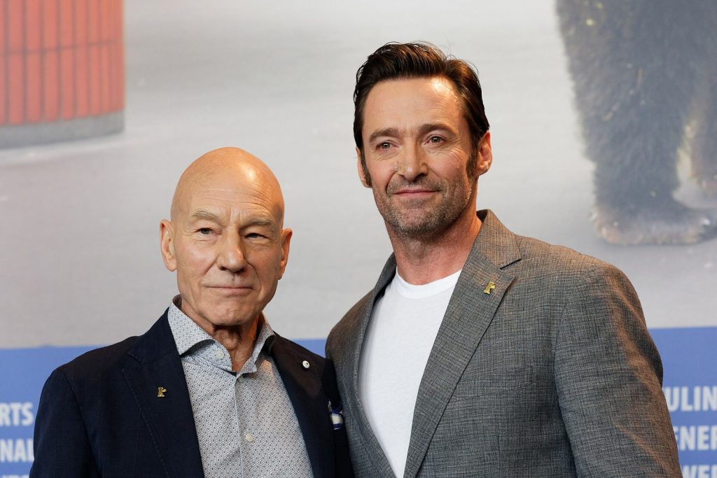 Patrick Stewart, en veste sombre et chemise grise, pose aux côtés de Hugh Jackman, en costume gris, devant un panneau de la Berlinale.