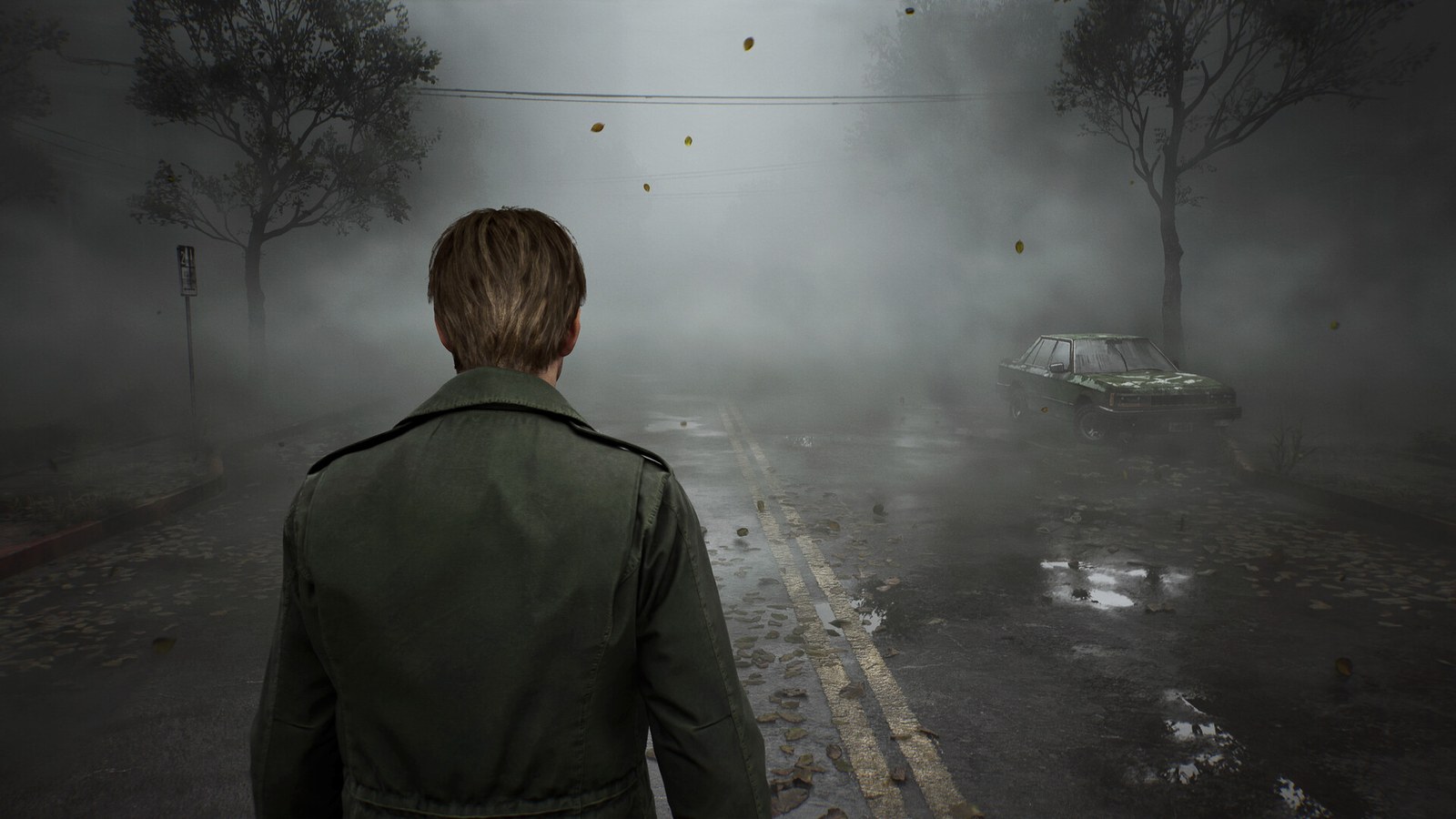 Dans le remake de Silent Hill 2, James Sunderland, vu de dos en veste verte, avance dans une rue couverte de feuilles mortes et noyée de brouillard, vers une voiture abandonnée.