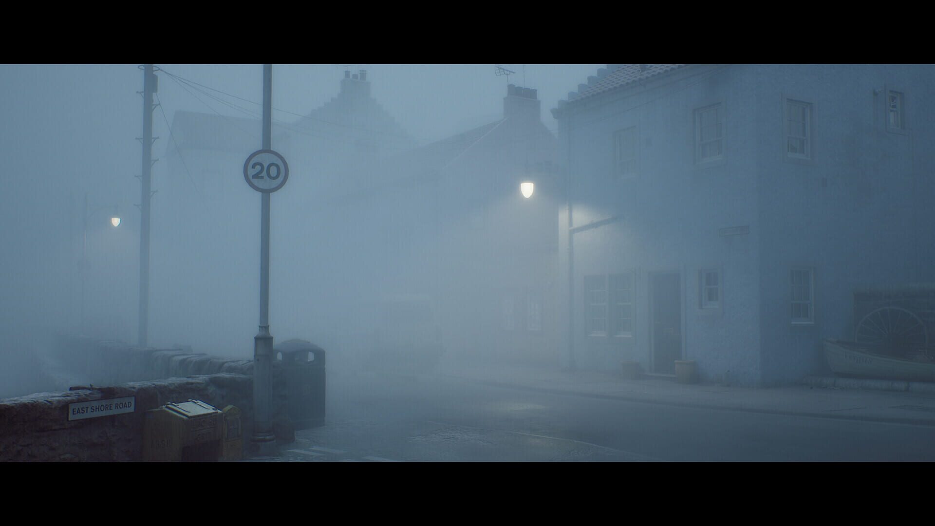 Une rue de village écossais noyée dans un brouillard épais, lampadaires allumés et panneau de limitation à 20.